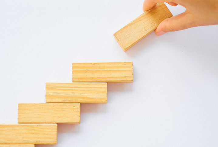 Person with white hand placing one wooden block on top of five others in a stair formation.