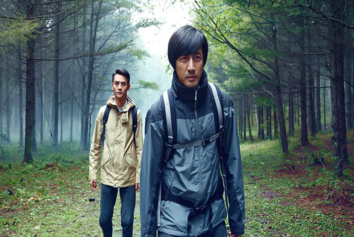 Two Asian men wearing rain jackets walkning on forest path