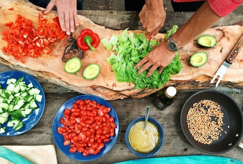 Two pairs of hands from above preparing food with many fresh ingredients