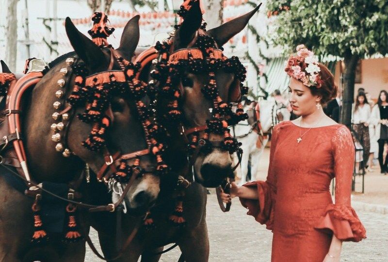 A woman in a red Flamenco style dress stands by a horse