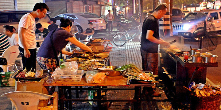 Three people preparing and grilling Chinese barbeque on the street