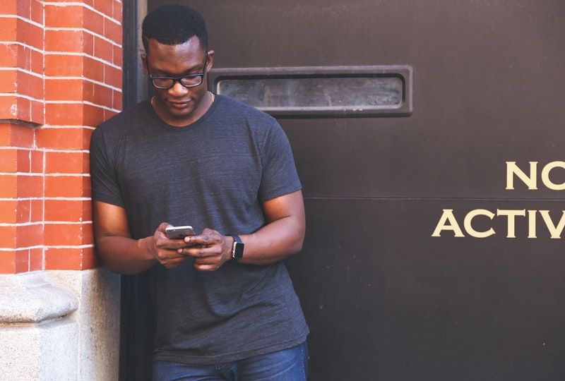 man using smartphone next to a brick building