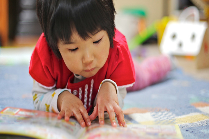 Asian child in red t-shirt reading on the floor