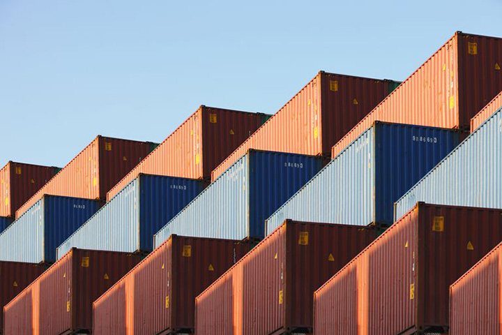 Three rows or brown, blue and red frieght containers under a blue sky