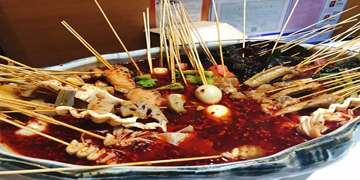 Skewers of meat and vegetables including eggs, lotus root, tofu and mushroom in a bowl of spicy red oil