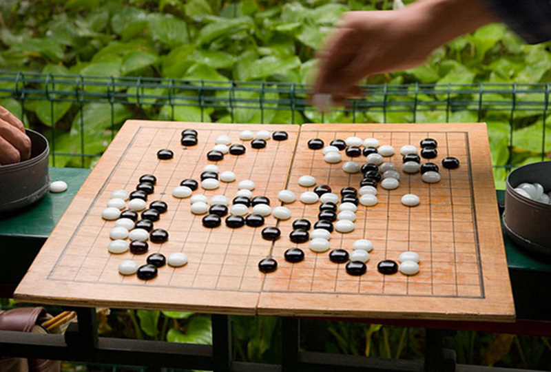 White and black pebbles on a brown wooden board with black squares in a garden