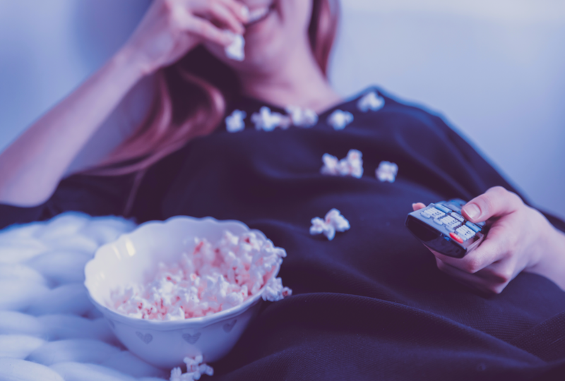 Woman eating popcorn and holding television remote